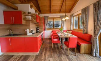 Modern kitchen with red cabinets and a wooden dining table. Large windows provide plenty of natural light and a cozy atmosphere.