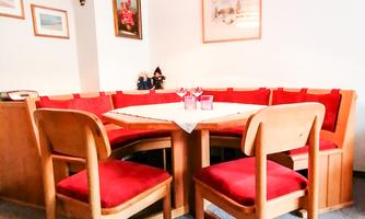 A cozy dining area with a round table and red upholstered chairs. The walls are decorated with pictures, and a lamp provides warm light.
