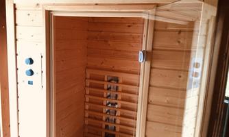 A modern wooden sauna with a glass door. Inside, wooden shelves and controls are visible.