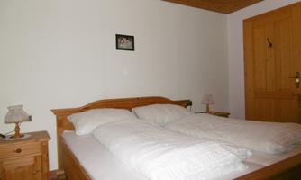 A simple bedroom with a double bed and two nightstands. The walls are light, and a door is visible.