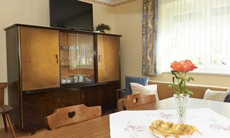 A cozy living space with an elegant cabinet and a dining table. On the table, there is a vase with a rose and a decorative plate.