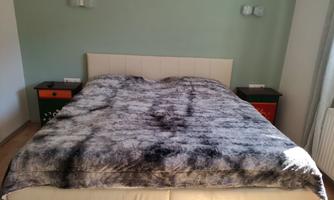 A bedroom with a large bed and a gray blanket. On the sides, there are two nightstands.