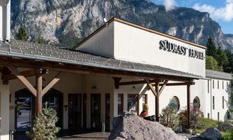 A hotel building with the inscription "Südrast Hotel" and a rocky facade. In the background, high mountains and a clear blue sky are visible.
