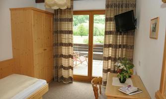 A cozy room with a single bed, a table, and chairs. Large windows overlooking nature allow plenty of light in.