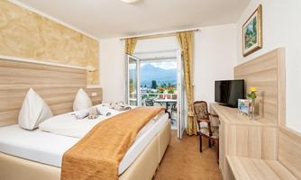 A cozy hotel room with a double bed and two pillows. The room has large windows with a view of the mountains and is furnished with modern decor.