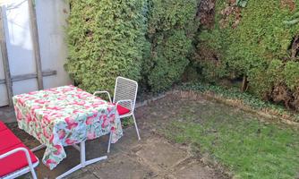 A small garden with grassy areas and hedges. A table with a floral tablecloth and two chairs invites you to linger.