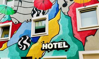A colorful mural with umbrellas and musical notes adorns the facade of a hotel. The vibrant colors and shapes make the building eye-catching and inviting.