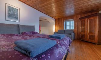 A cozy bedroom with wooden walls and a double bed. There is a desk and a wardrobe in the room.