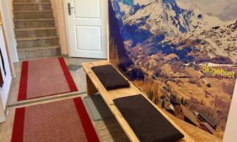 A cozy entryway with a wooden bench and red carpets. On the wall, there is an impressive photo of snow-covered mountains and a ski resort.