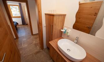 A modern bathroom with an oval sink and wooden cabinet. In the background, there is a room with a window and a wooden door.