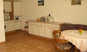 A bright kitchen with modern furniture and a round table. The walls are light, and the floor is tiled.