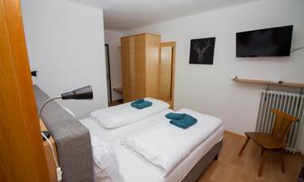 A cozy bedroom with two single beds and fresh towels. The room is bright and modernly furnished, with a TV and a chair.