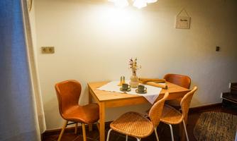 A cozy dining area with a wooden table and chairs. On the table, there are cups and a small vase with flowers.