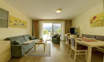 A modern living room with a cozy couch and a dining table. Large windows offer a beautiful view of the mountains.
