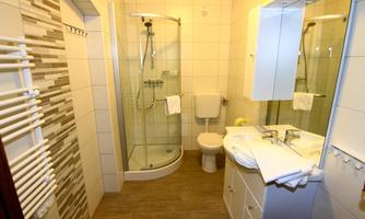 A modern bathroom with a shower, toilet, and sink. The walls are brightly tiled, and there are towel holders.