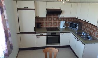 A modern kitchen with bright cabinets and a dining area. The kitchen appliances are neatly arranged and the walls are decorated with orange tiles.