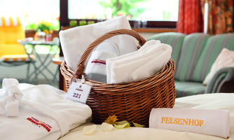 A basket with towels and bathrobes on a bed. In the background, there is a cozy room with natural light.