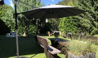 A beautiful garden with a large sun umbrella and garden furniture. In the background, there are lush trees and plenty of greenery.