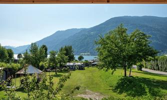 A picturesque landscape with green grass and trees. In the background, gentle mountains and a shimmering lake can be seen.