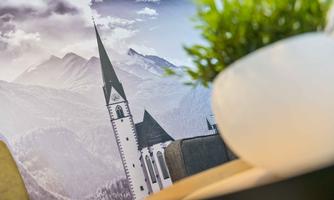 A beautiful picture of a church with a tall steeple set against a mountainous landscape. In the foreground, a green plant basket is visible.