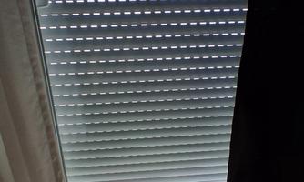 A window view with blinds and a floor made of light wood. A black curtain is also visible.