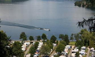 A beautiful lake with a boat and water activities. In the foreground, there is a campsite with many caravans.