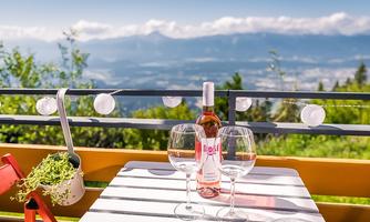 A table on a balcony overlooking the mountains. On it are a bottle of rosé wine and two wine glasses.