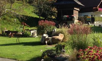 A beautiful garden with colorful flowers, stones, and decorative sculptures. In the background stands a traditional wooden building.