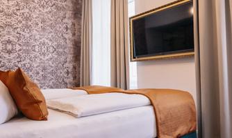 A modern hotel room with a comfortable bed and elegant decoration. A flat-screen TV is mounted on the wall next to large windows with curtains.