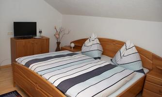A cozy bedroom with a large bed and striped bedding. Next to the bed is a television and a simple flower decoration.