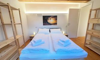 A modern bedroom with a double bed and two bunk beds. There are warm wooden tones and a painting on the wall.