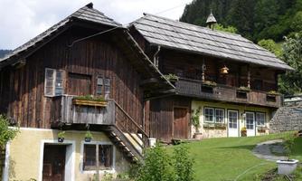 A traditional wooden house with a steep roof and green grass. Surrounded by trees and a peaceful landscape.