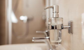 A modern sink with a clear soap dispenser and chrome-plated fittings. The background is blurry and conveys an elegant bathroom style.