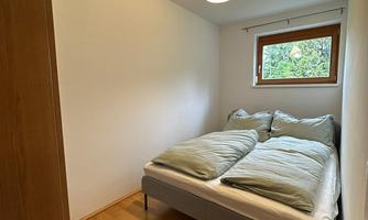 A simple bedroom with a double bed and light wooden flooring. The window offers views of the outdoors and lets in plenty of light.