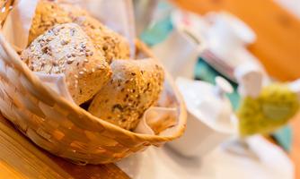 A basket of fresh rolls, sprinkled with seeds. In the background, breakfast utensils are visible.