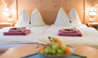 A cozy room with two beds and pillows. On the table, there is a bowl of fresh fruit.