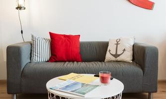A stylish living room with a gray sofa, colorful cushions, and a round coffee table. Red oars hang on the wall, and a lantern provides cozy light.