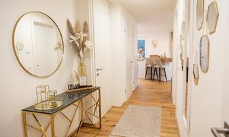 A modern hallway with an elegant table, a round mirror, and decorative plants. Bright walls and wooden flooring create an inviting atmosphere.