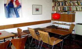 A modern living room with wooden shelves and a round red lampshade. There are wooden furniture and a carpet on the floor, creating a cozy atmosphere.