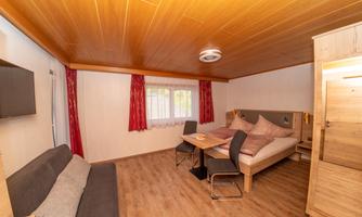 A cozy room with a double bed, a sofa, and a table. Large windows provide plenty of daylight.