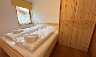 A cozy bedroom with a double bed and fresh towels. The room is bright and has a wooden cupboard on the wall.