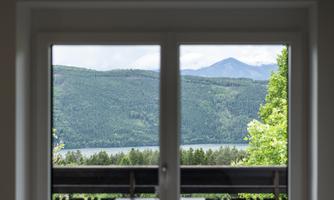 A balcony with a table and chairs that offers a view of green mountains and a lake. The view is clear and inviting.