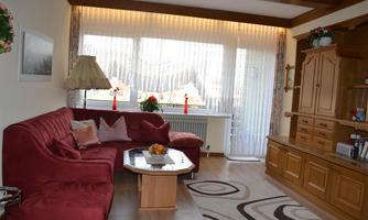 A cozy living room with a red sofa and a wooden furniture wall. Large windows let in plenty of light and create an inviting atmosphere.