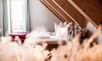 A cozy bedroom with a large bed and wooden details. Bright curtains let in plenty of light and create an inviting atmosphere.