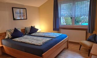 A cozy bedroom with a double bed and bright walls. The room is furnished with a chair and a beautiful view of nature.