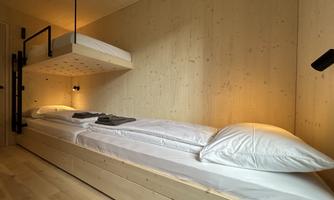 A modern bedroom with a low bed and a lofted sleeping area. The walls are made of light wood, and there is soft lighting.