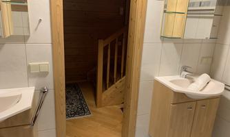 A modern bathroom with wood and tiled cladding. In the background, a staircase is visible, leading to additional rooms.