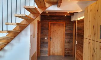 A modern hallway with a wooden staircase and rustic wooden walls. The doors are made of light wood, and the room has an inviting atmosphere.