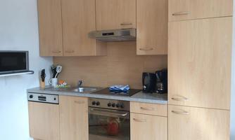 A modern kitchen with wooden cabinets and a stone countertop. It includes essential kitchen appliances such as a stove, a microwave, and coffee machines.