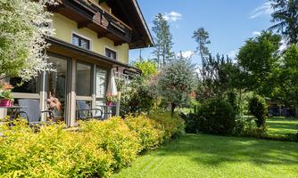 A charming house with a beautiful garden and green plants. The terrace is inviting and surrounded by trees.